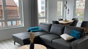 Ein modernes Wohnzimmer mit einem grauen Ecksofa, einem runden Couchtisch und einem Essbereich mit Holztisch und Stühlen.