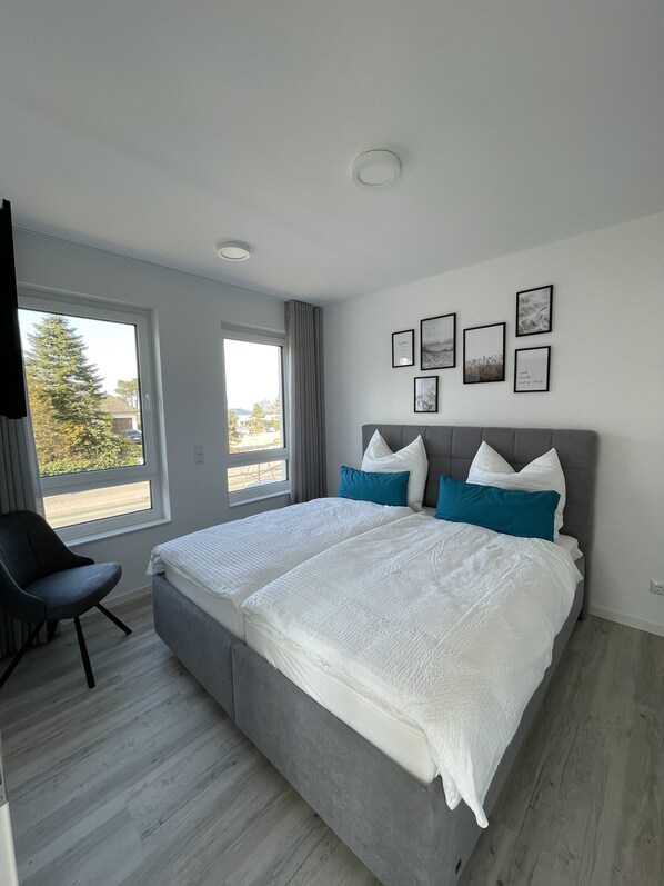 Ein modernes Schlafzimmer mit einem großen Bett, einem Sessel und einem Fenster mit Blick.