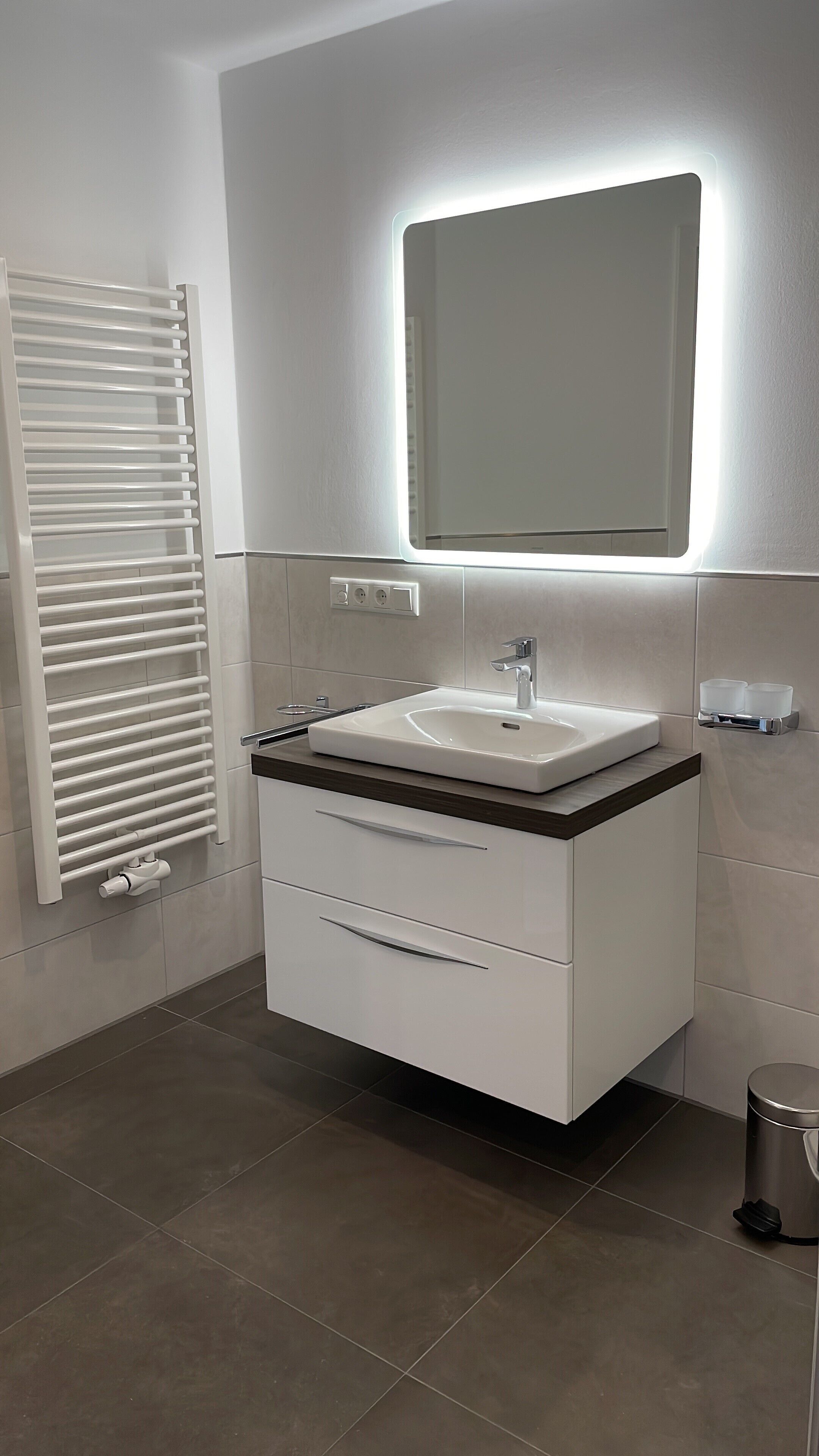 Une salle de bain moderne avec un lavabo blanc, un miroir et un porte-serviettes.