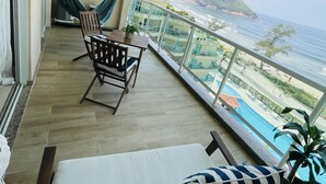 Un balcone con tavolo e sedie in legno, un'amaca e vista sull'oceano e su una montagna.