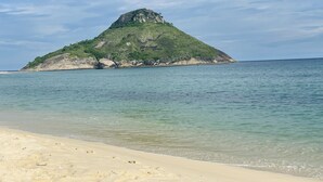 Una spiaggia con acque limpide e una piccola isola con terreno roccioso e vegetazione.