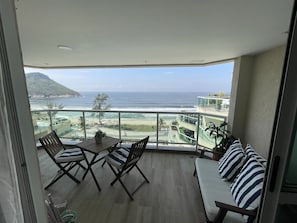 Varanda com vista para o oceano e a praia, mobiliário de madeira e um vaso de planta.
