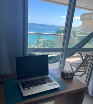 Un ordinateur portable est posé sur un bureau près d’une fenêtre donnant sur l’océan.