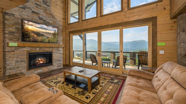 A cozy living room with a stone fireplace, comfortable seating, and large windows offering mountain views. - Priceless Views, Indoor Pool Firepit Pool Table, Hot Tub, & Free Attractions! (Gatlinburg)