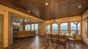 A spacious room with a wooden floor, a stone fireplace, a sofa, and a dining table with chairs. - Priceless Views, Indoor Pool Firepit Pool Table, Hot Tub, & Free Attractions! (Gatlinburg)