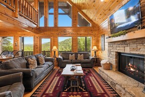A log cabin interior with a fireplace, a large TV, and a cozy seating area.