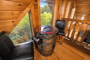 A wooden interior with a barrel table, two chairs, and a view of greenery outside.