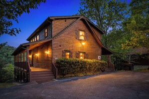 A log cabin with a porch, a staircase, and a well-lit exterior.