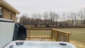 Un jacuzzi en una terraza de madera con vistas a un campo cubierto de césped y árboles al fondo.