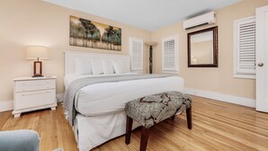 A bedroom with a bed, bedside table, lamp, and a painting on the wall. - Walk to the Waves- Gorgeous Carillon Beach Bungalow (Panama City Beach)