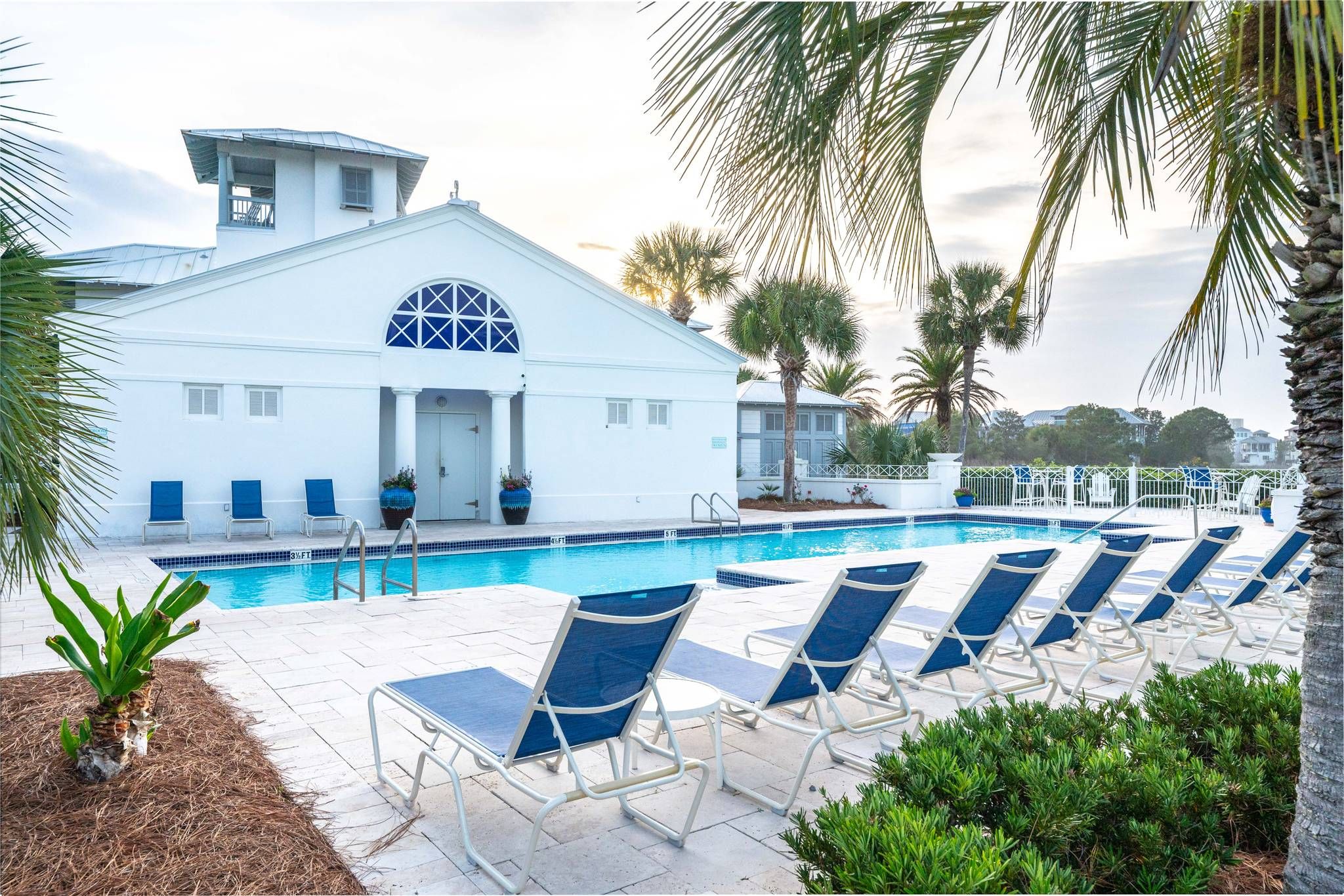 A white building with a pool and lounge chairs.