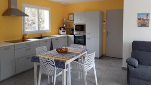 A compact kitchen with white cabinets, a microwave, and a stove. There is a dining table with a basket and a colorful tablecloth. - New comfortable house with swimming pool in Provence (Régusse)