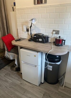 Une petite cuisine équipée comprenant un plan de travail, un petit réfrigérateur, une poubelle et un radiateur portatif.