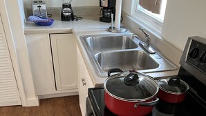 Una cocina compacta con estufa, pileta y tostadora. Hay ollas en la estufa y una cafetera en la encimera.