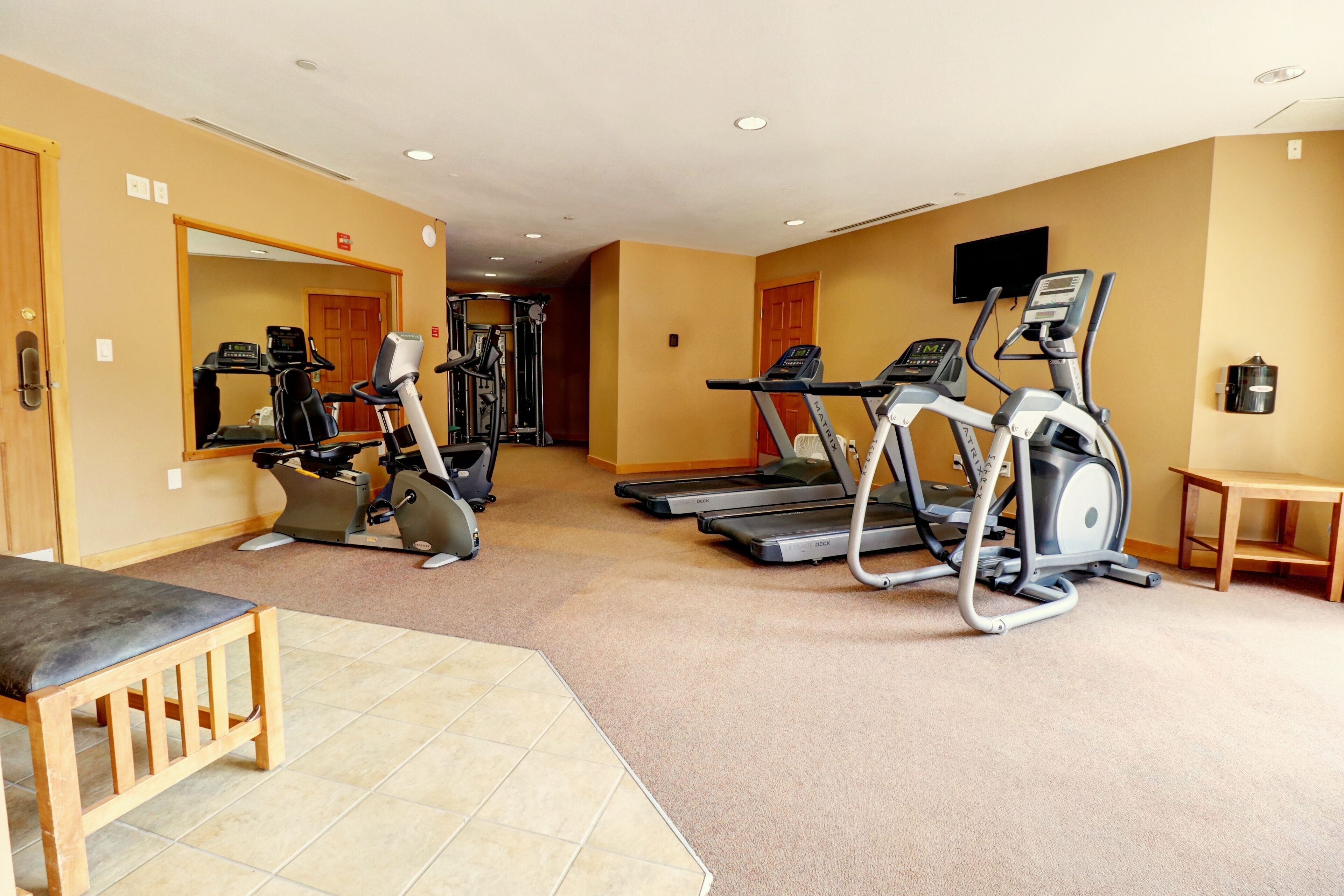 Une salle de sport équipée de tapis de course, d’un vélo elliptique et d’un banc de musculation.
