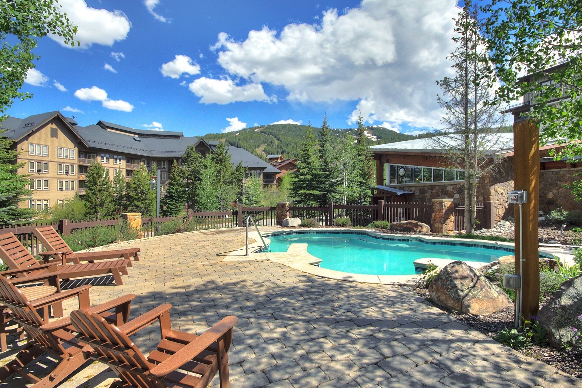A pool area with lounge chairs, a stone patio, and a view of mountain buildings.