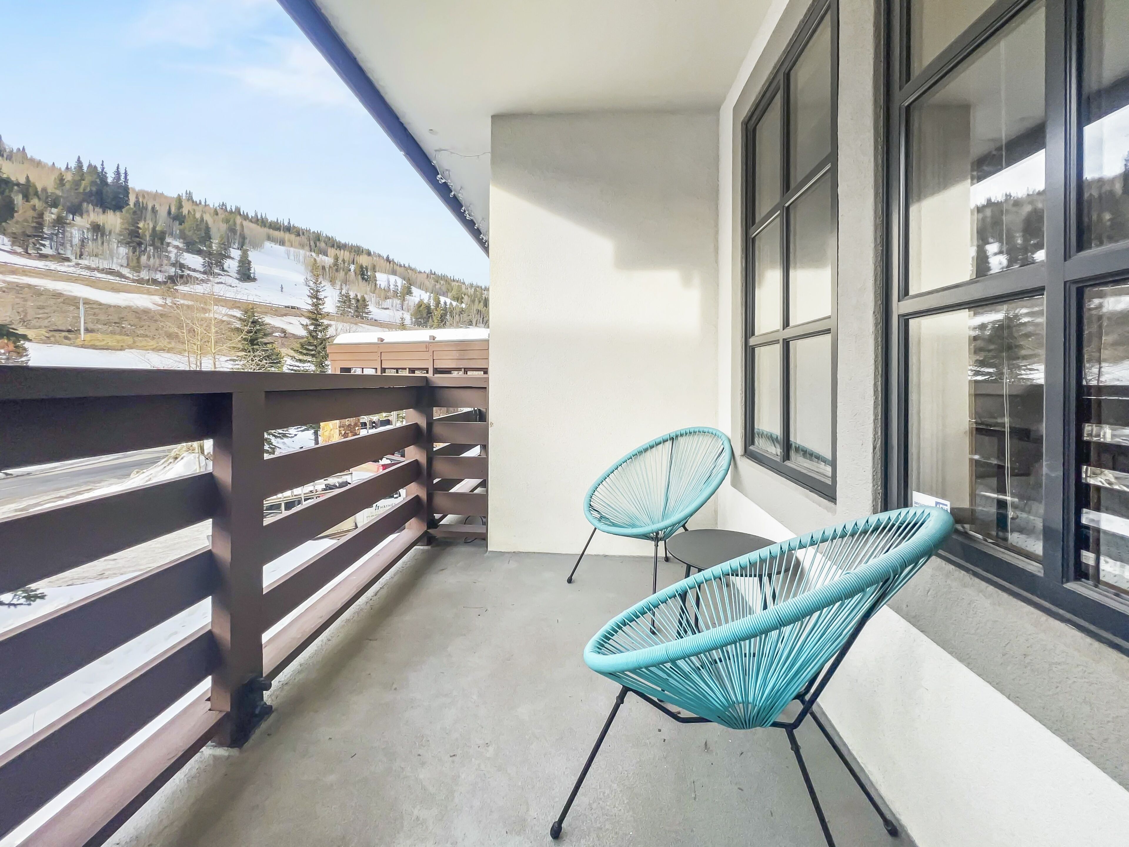 Un balcon donnant sur un paysage enneigé, deux chaises turquoise et un sol en béton.