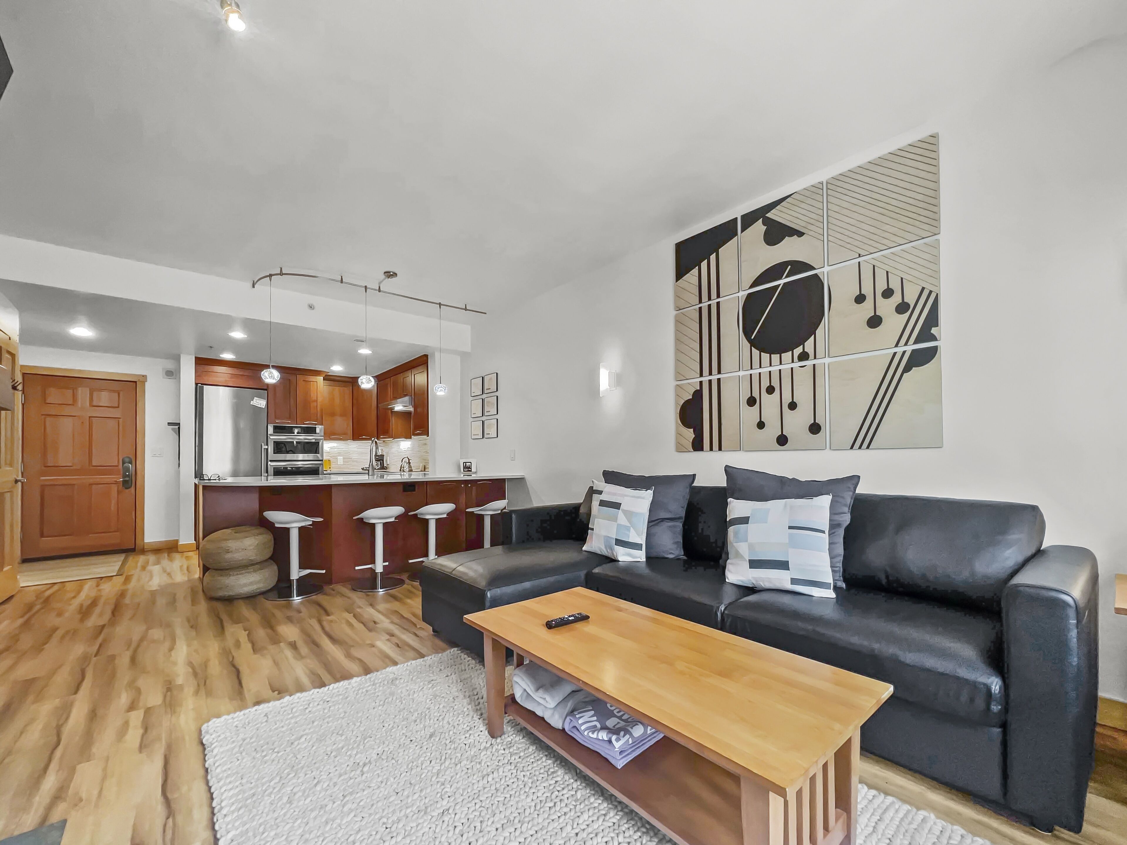 A modern living room with a black sofa, wooden coffee table, and a kitchen in the background.
