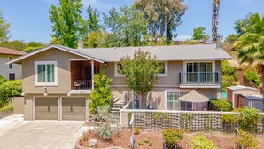 A two-story house with a front porch, a garage, and a landscaped garden with various plants and a small tree. - Private Entry Elegant Quiet Safe Cozy Studio Suite  (Pleasant Hill)