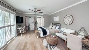 A spacious living room with a large window, a ceiling fan, a bed with a white headboard, a white sofa, and a round coffee table. - Private Entry Elegant Quiet Safe Cozy Studio Suite  (Pleasant Hill)