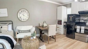 A modern living room with a round coffee table, a sofa, a dining area, and a kitchen with a refrigerator and microwave. - Private Entry Elegant Quiet Safe Cozy Studio Suite  (Pleasant Hill)