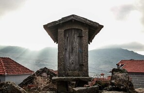 Une construction rustique en pierre, dotée d’une porte en bois, entourée d’un paysage rocheux et s’élevant sur un fond de montagnes.