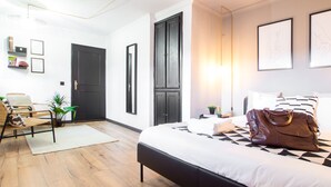 Camera d'albergo moderna con un grande letto, una scrivania e una sedia. Si notano due porte, una finestra e una parete con opere d'arte incorniciate.