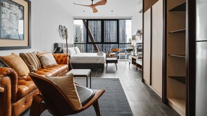 Een moderne hotelkamer met een groot bed, een leren zithoek, een eethoek en uitzicht op de skyline van de stad.
