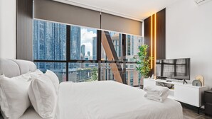 Een moderne hotelkamer met een groot bed, een flatscreen televisie en een uitzicht over de stad door middel van kamerhoge ramen.