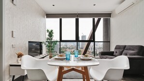 Een moderne eethoek met een groot raam, twee witte stoelen, een gedekte tafel met borden en glazen, en een donkere bank op de achtergrond.
