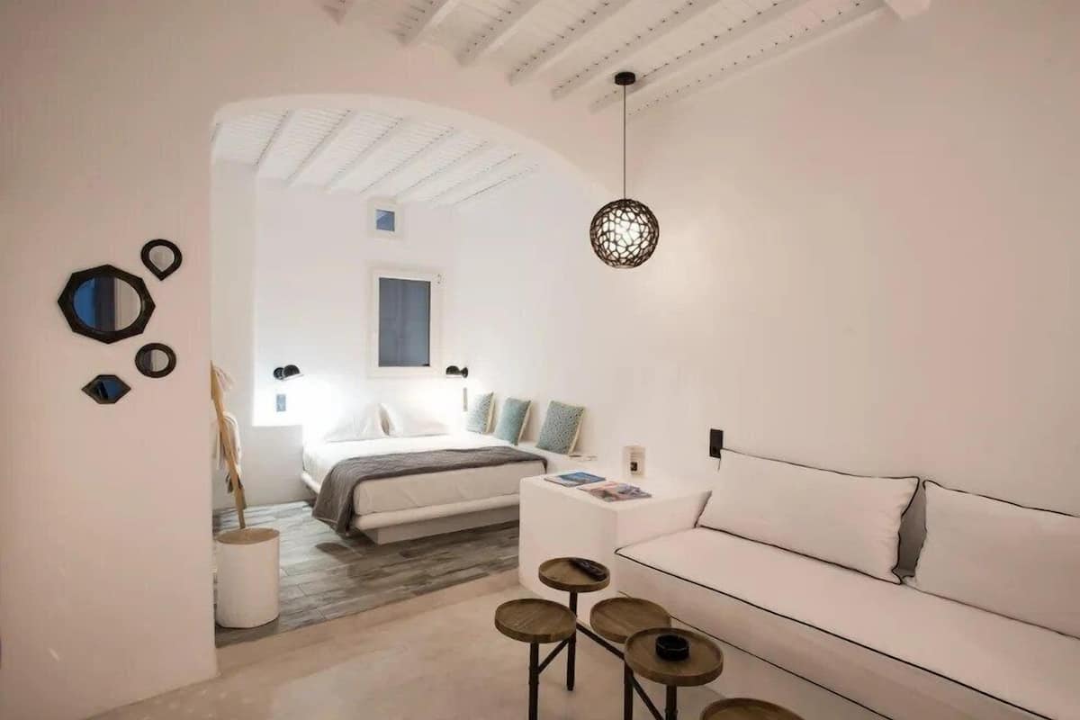 A modern bedroom with a bed, a white sofa, a small table, and a hanging light fixture.