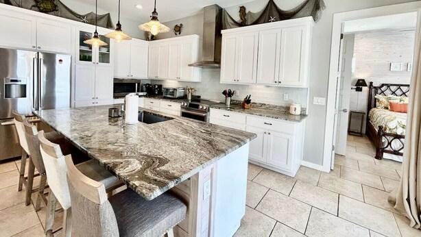 Una cocina moderna con armarios blancos, una isla grande con taburetes de bar e iluminación colgante.
