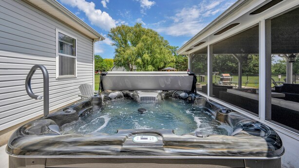 Un jacuzzi en un patio trasero, con una casa a un lado y un porche cubierto al otro.
