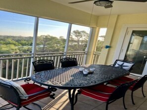 Een balkon met een ronde metalen tafel, rode stoelen met kussens en uitzicht op groen.