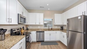 A modern kitchen with white cabinets, stainless steel appliances, and a granite countertop. - Stylish New Build! 2BR Condo w/ Patio & Garage (Wyoming)
