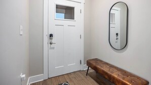 A white door with a window, a bench, and a mirror on the wall. - Stylish New Build! 2BR Condo w/ Patio & Garage (Wyoming)