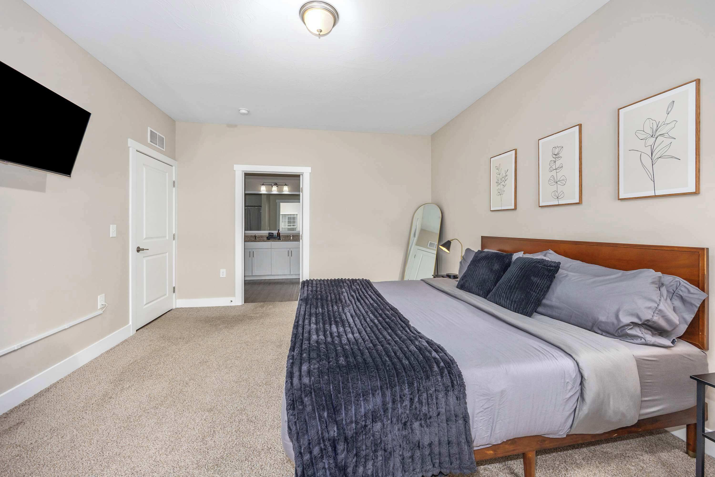 A bedroom with a bed, a bedside table, a wall-mounted TV, and framed artwork.