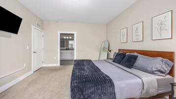 A bedroom with a bed, a bedside table, a wall-mounted TV, and framed artwork.