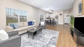 A spacious living room with a sofa, coffee table, and TV stand, a dining area with chairs and a table, and a kitchen with cabinets and appliances. - Stylish New Build! 2BR Condo w/ Patio & Garage (Wyoming)