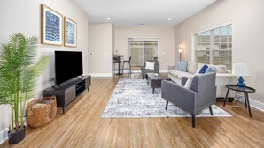 A modern living room with a flat-screen TV, grey sofa, and a coffee table. - Stylish New Build! 2BR Condo w/ Patio & Garage (Wyoming)