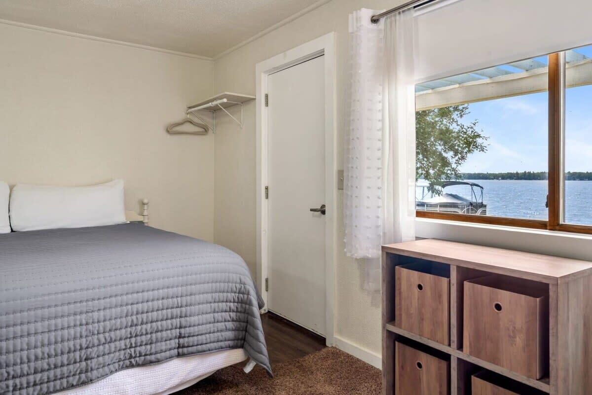 Quarto com cama, porta, janela com vista para um lago e um armário de madeira.
