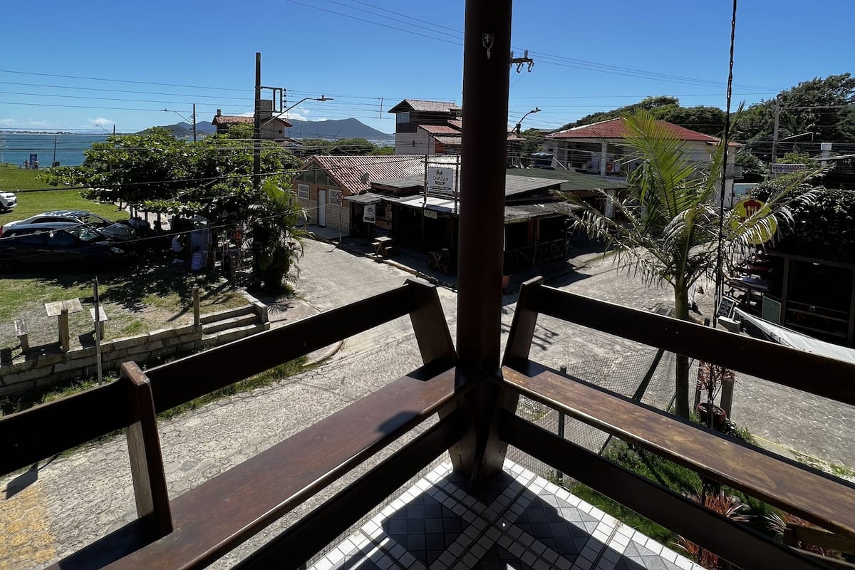 A balcony with a tiled floor and wooden railings overlooking a street with buildings and a clear blue sky.