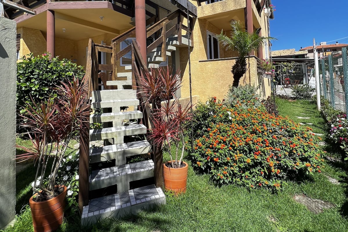 A multi-story building with a wooden staircase leading to a balcony, surrounded by potted plants and a well-maintained garden.