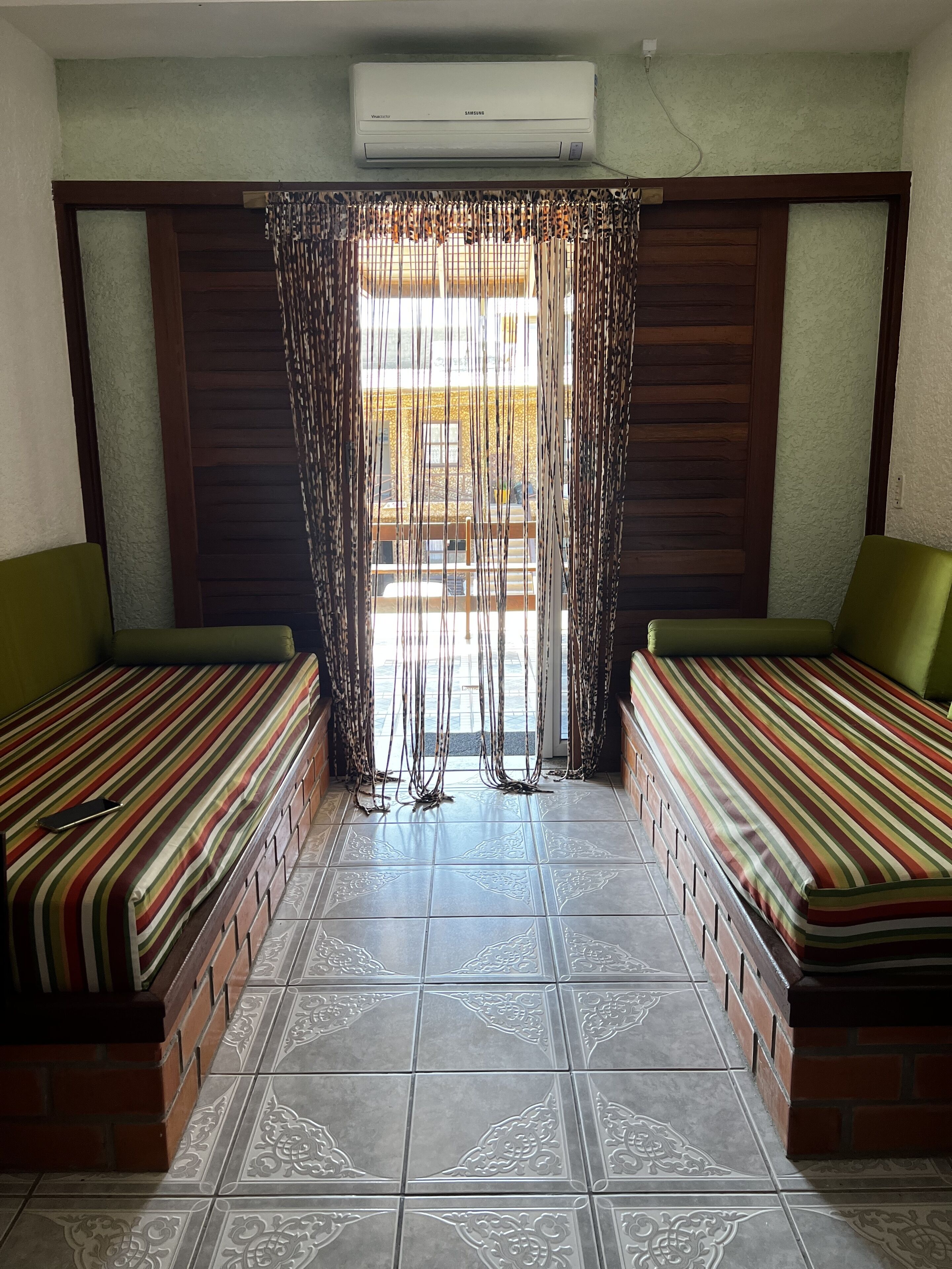 A room with two single beds, a window with curtains, and an air conditioning unit.