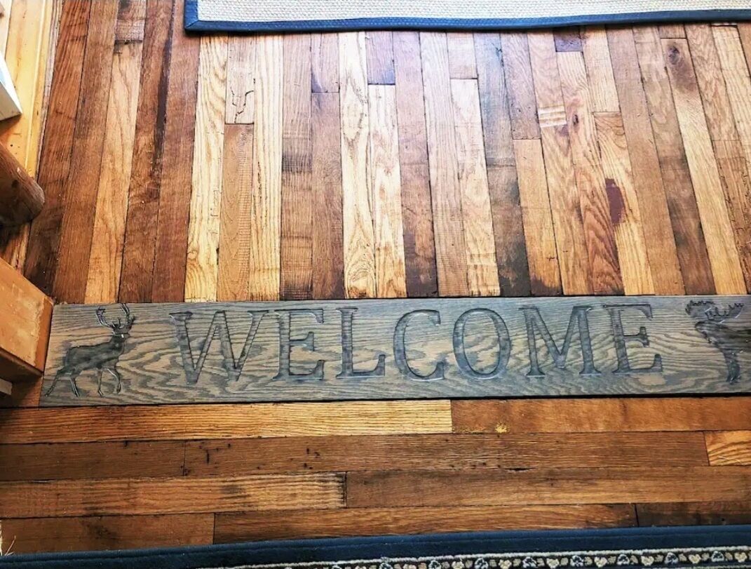 A wooden welcome sign with deer silhouettes and the word "WELCOME" engraved on it.