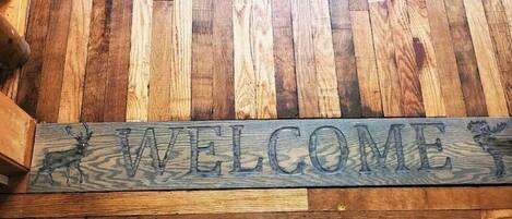 A wooden welcome sign with deer silhouettes and the word "WELCOME" engraved on it.
