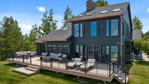 Une maison moderne à deux étages, dotée d’une terrasse, de grandes fenêtres et d’une cheminée en pierre.