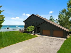 A two-story house with a sloped roof, a garage, and a large front porch. - Loeb Lake House - sugar sand private beach - walking distance to Castle Farms (Charlevoix)