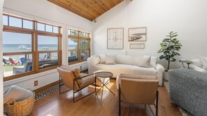 Un salon spacieux doté d’une grande fenêtre donnant sur une terrasse et la mer. On y trouve un coin salon confortable avec un canapé et des fauteuils, une petite table ronde et une plante en pot.