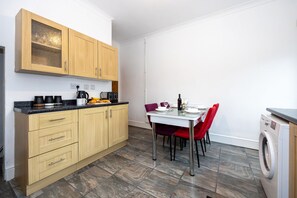 Una cocina compacta con armarios de madera, una mesa de comedor con sillas rojas y una lavadora.